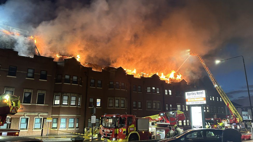 Night-time image of the roof of the police station on fire, with flames lighting up the sky and a turntable ladder being used to spray water from a height onto the blaze