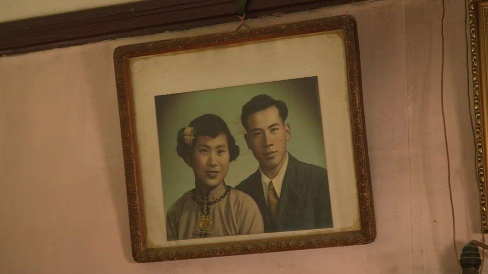 An old, sepia-toned picture of a Chinese couple, hanging on a wall.