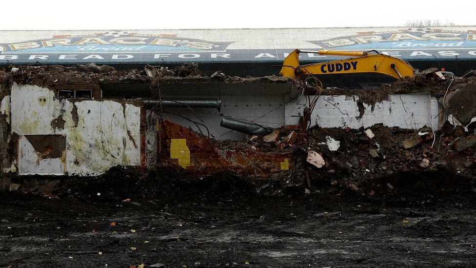 A yellow bulldozer stands out among the debris of Ninian Park football stadium's demolition