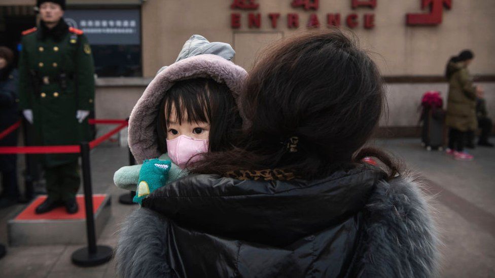 A Chinese girl wears a protective mask as she is held by a relative as they wait to board a train at Beijing Railway station