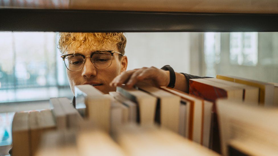 Young man searching through books in library at university