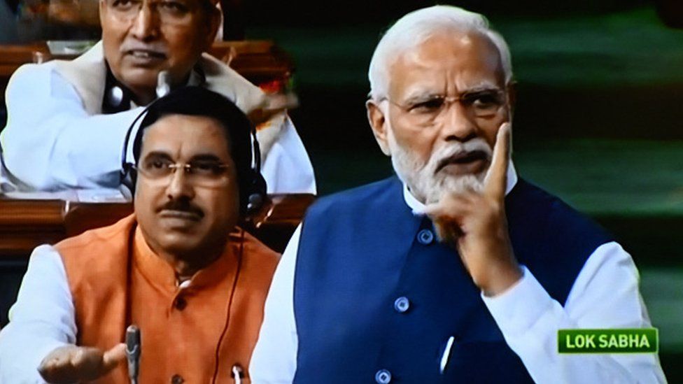 Премьер-министр Индии Нарендра Моди (справа) на экране телевизора выступает с речью перед нижней палатой Лок Сабха в Нью-Дели 10 августа 2023 года,