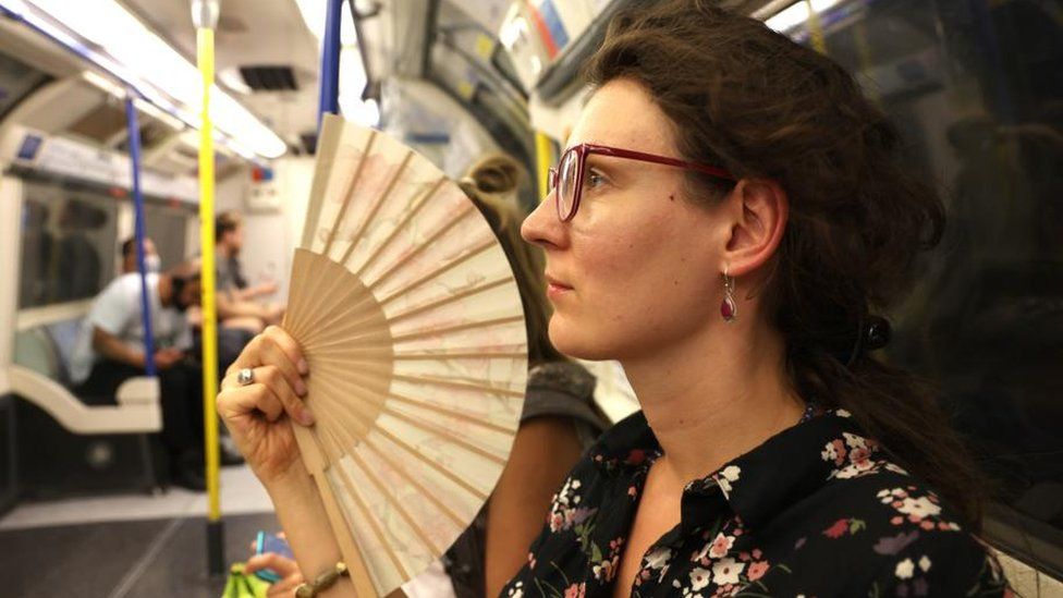 A woman uses a fan to cool herself in an underground train in London