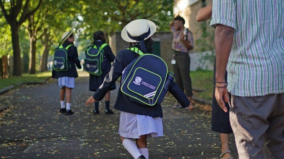 A young girl skips into the distance in her straw hat, uniform, and Corpus Christi-branded backpack.