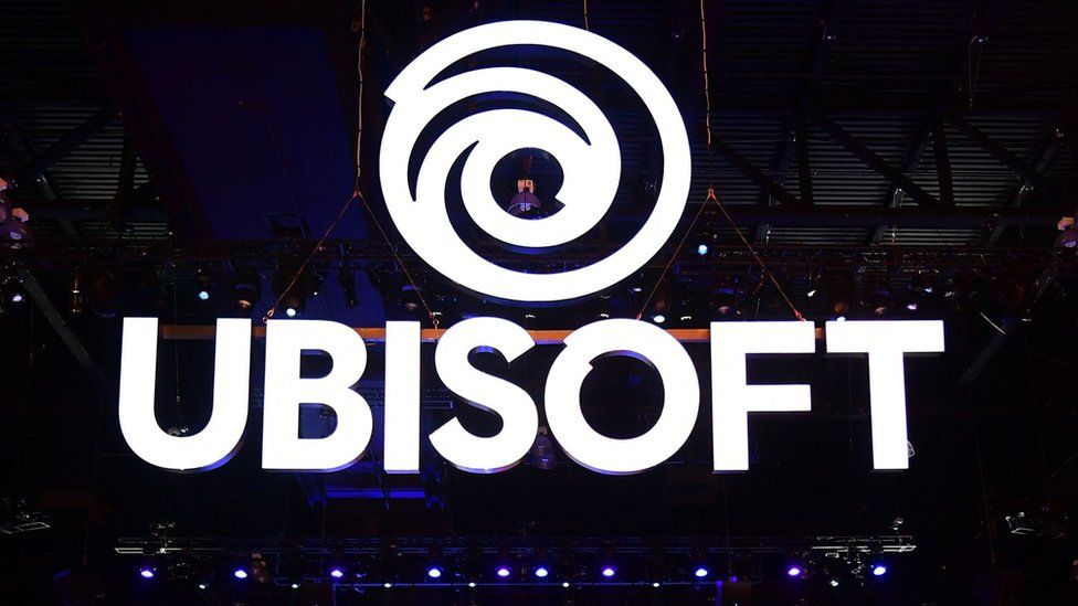 An enormous Ubisoft sign is suspended in the air at a busy trade show floor