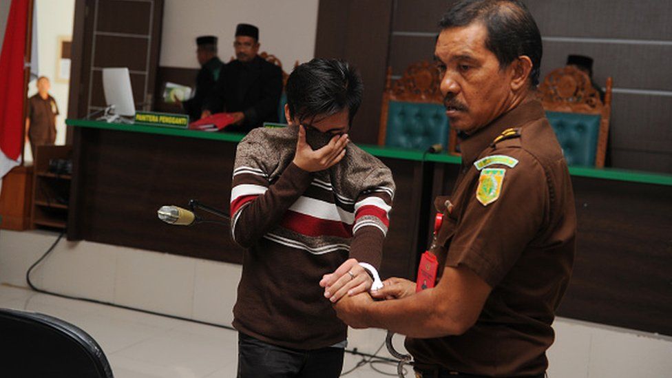An Indonesian official (R) escorts a man (L) after his trial at a sharia court in Banda Aceh on May 17, 2017
