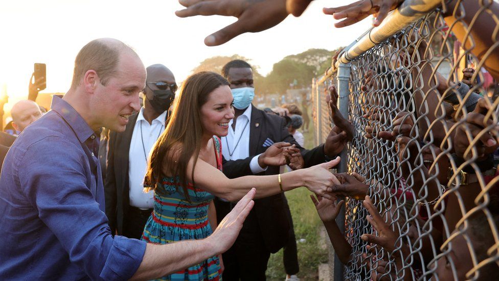 The Duke and Duchess of Cambridge reach through a metal fence to greet Jamaican children