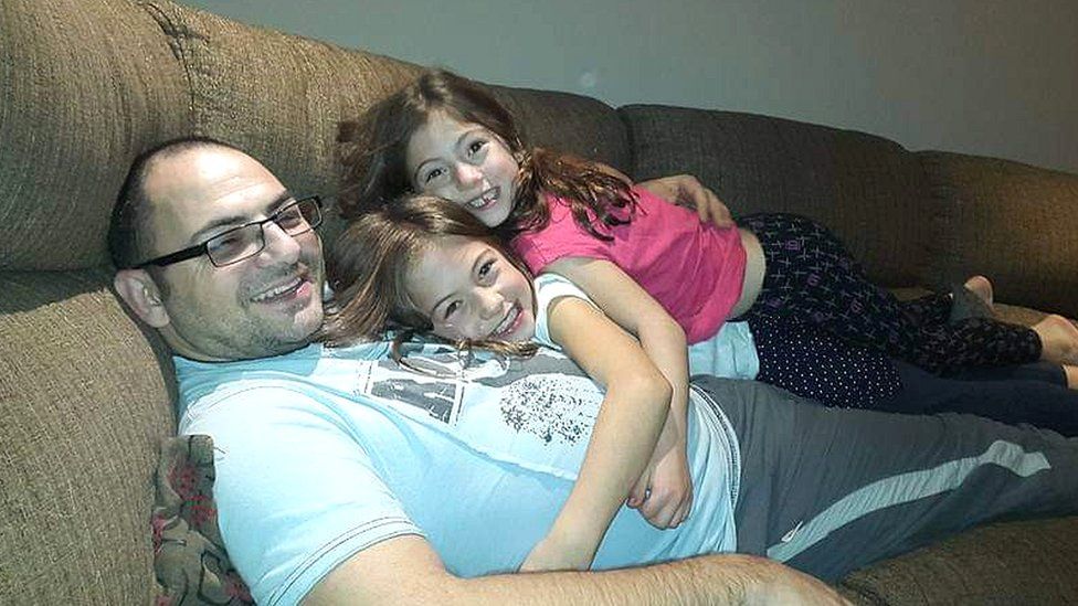 Neil Lanciano on a sofa with his two young daughters