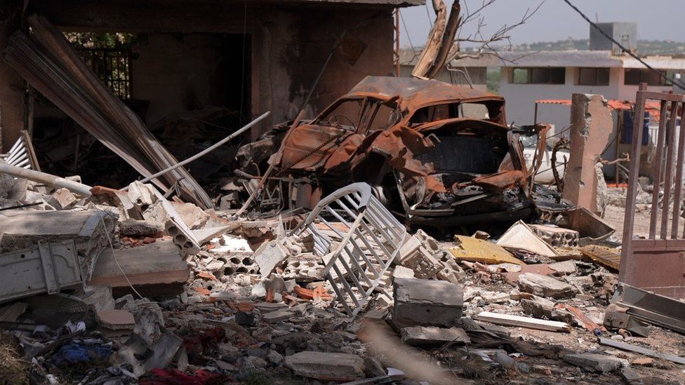 A damaged and rusted car surrounded by debris