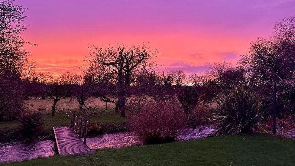 Pink and orange sky reflected in a stream in the foreground at Tarrant Monkton