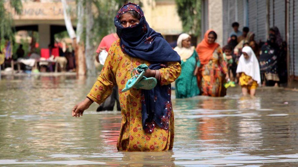 Люди идут по затопленной территории после проливных дождей в районе Даду, провинция Фарид Абад Синд, Пакистан, 27 августа 2022 г.
