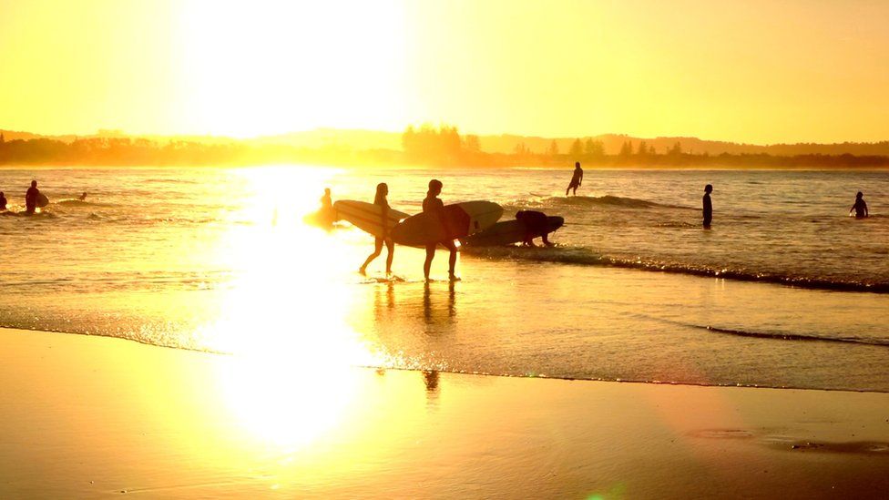 surfers walk into the water at sunset