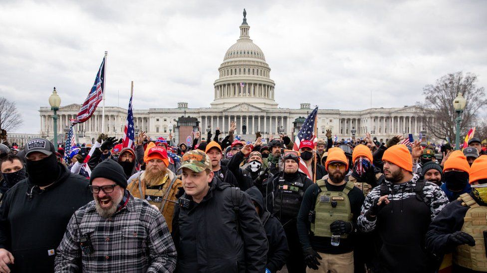 Proud Boys, many wearing orange hats, along with other rioters outside the US Capitol on 6 January 2021