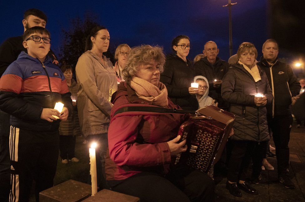 Marian Harper-Coleman plays her button accordion while other people hold candles during a vigil in Castlefinn