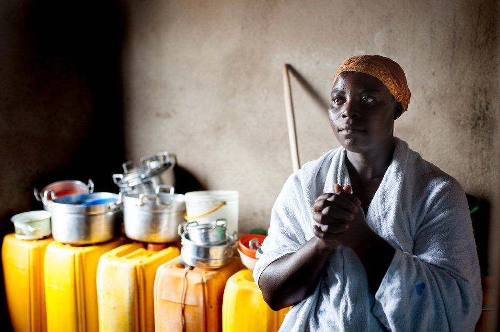 Hannah Abekah prays in front of the yellow buckets of rainwater she has collected