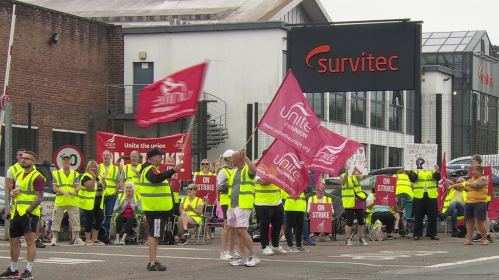 Survitec workers wave flags and hold placards on the picket line outside the company's Dunmurry factory