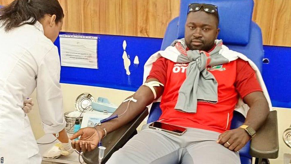 A member of the Gambian squad reclines and gives blood while a nurse works alongside him