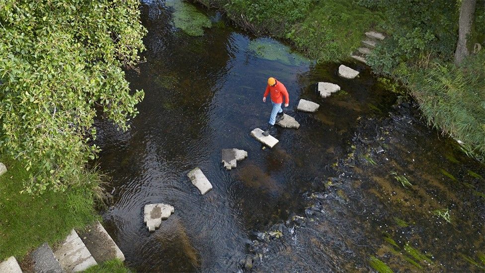 Man walking on stepping stones to cross river