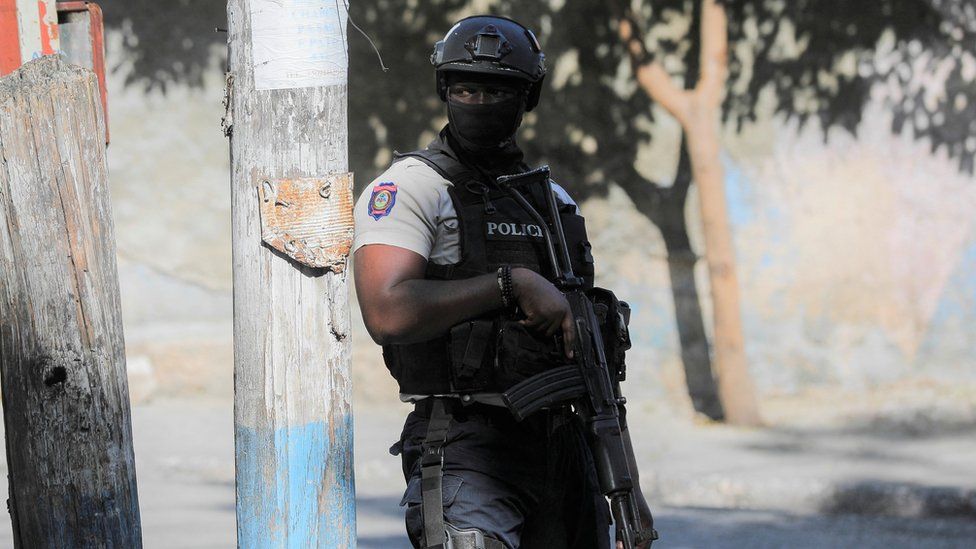 Офицер полиции стоит на страже возле места, где толпа людей подожгла предполагаемых членов банды в Порт-о-Пренсе