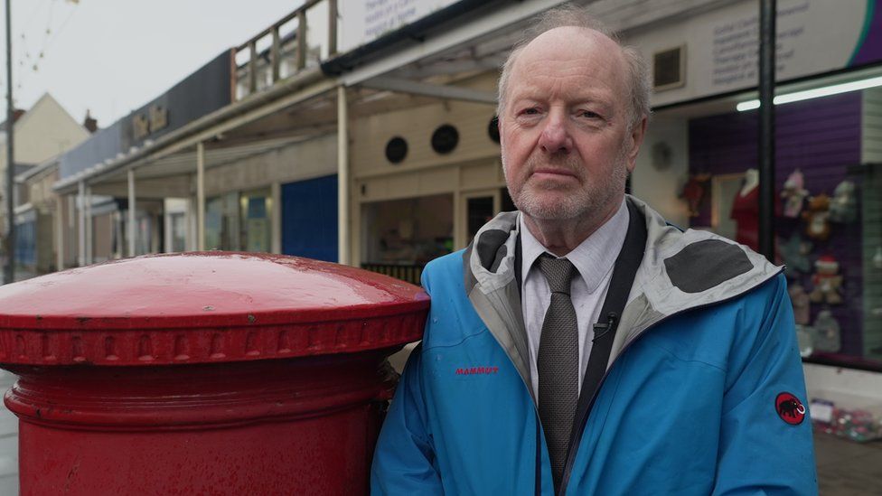 Post Office campaigner Alan Bates stands next to a post box