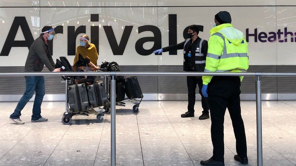 Passengers are escorted through the arrivals area of Heathrow Terminal Five, towards coaches destined for quarantine hotels