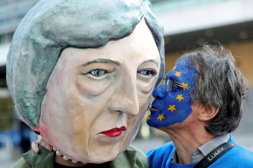 An anti-Brexit protester kisses a Theresa May head before a summit in Brussels