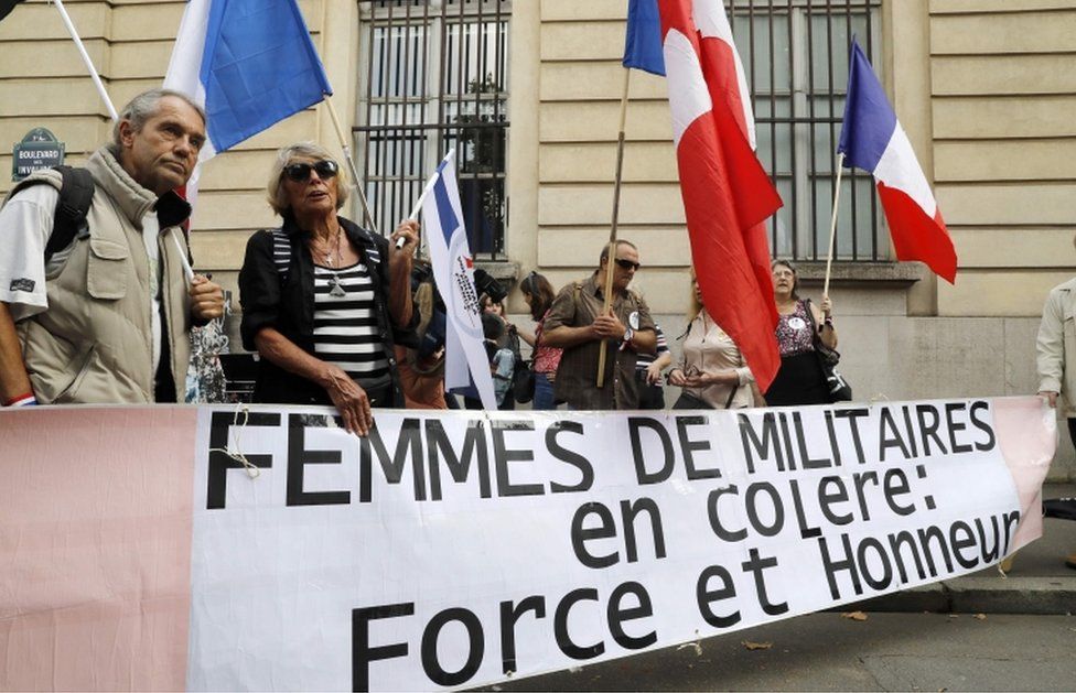 Members and supporters of the collective "Military spouses are angry" hold flags and a banner during a demonstration