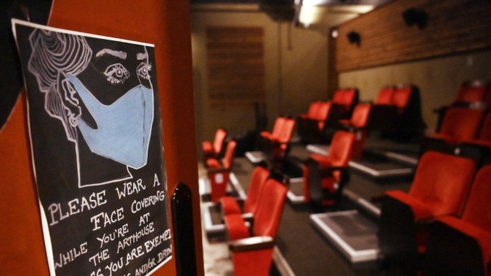 Табличка с просьбой к покупателям носить маску в пустом кинозале с удаленными сиденьями в Лондоне