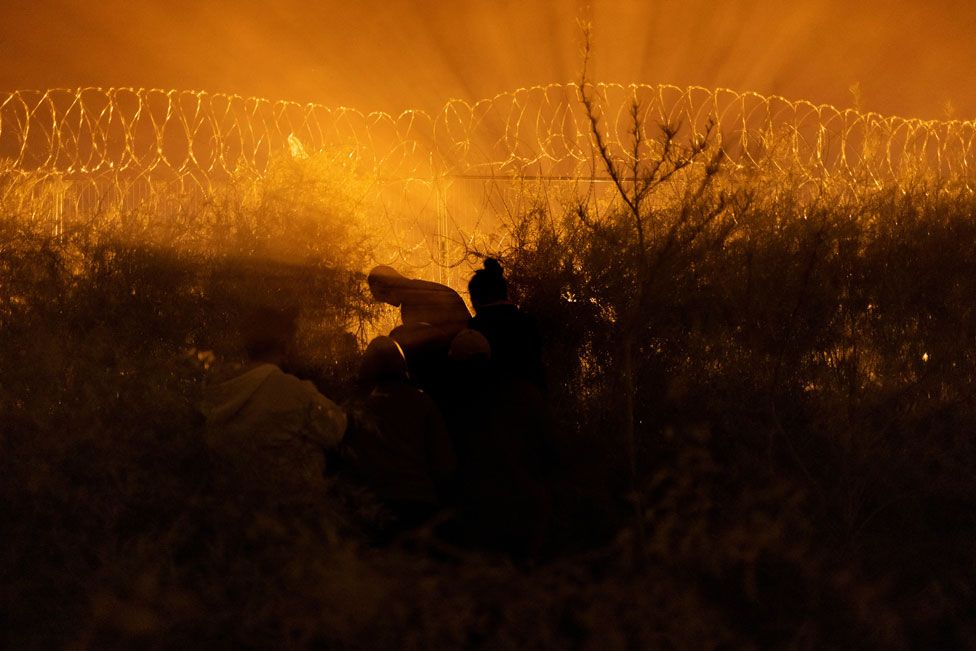A man shears an opening through a razor wire-laden fence for a group of migrants from South and Central America as they prepare to enter into the United States from along the bank of the Rio Grande river, in El Paso, Texas, U.S., March 27, 2024.