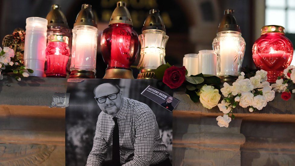 A photograph of Pawel Adamowicz is pinned to a ledge filled with flowers and candles