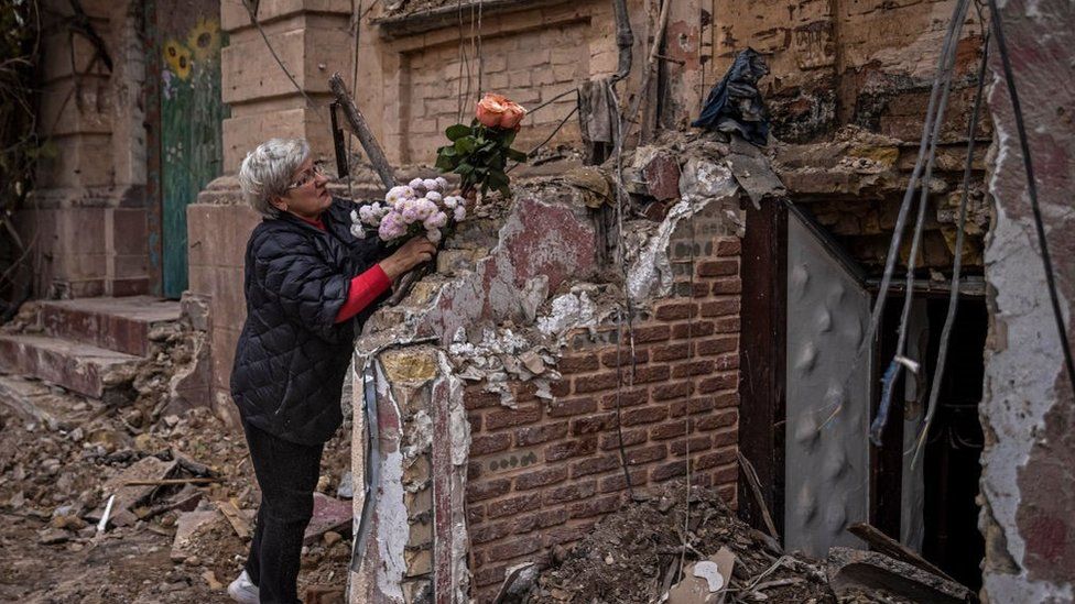 A woman arranges flowers outside a house where a couple was killed in a Russian drone strike two days beforehand on October 19, 2022 in Kyiv