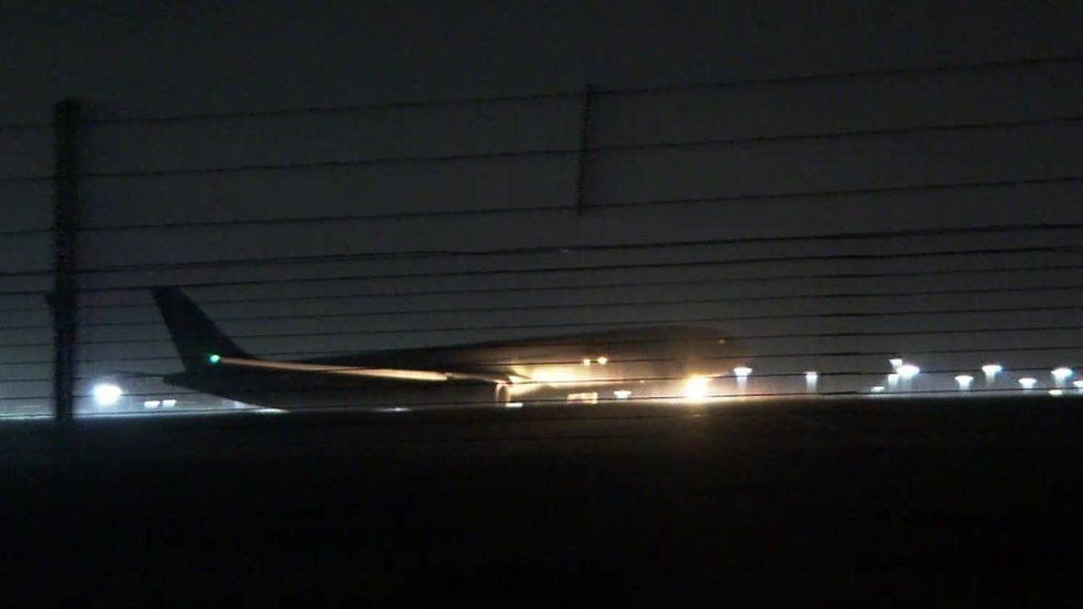 A plane is seen through an airport fence landing at night