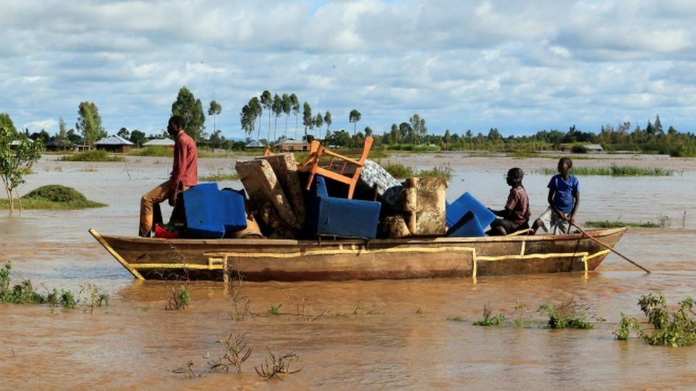 Residents use a boat to carry their belongings through the waters after their homes were flooded as the River Nzoia burst its banks