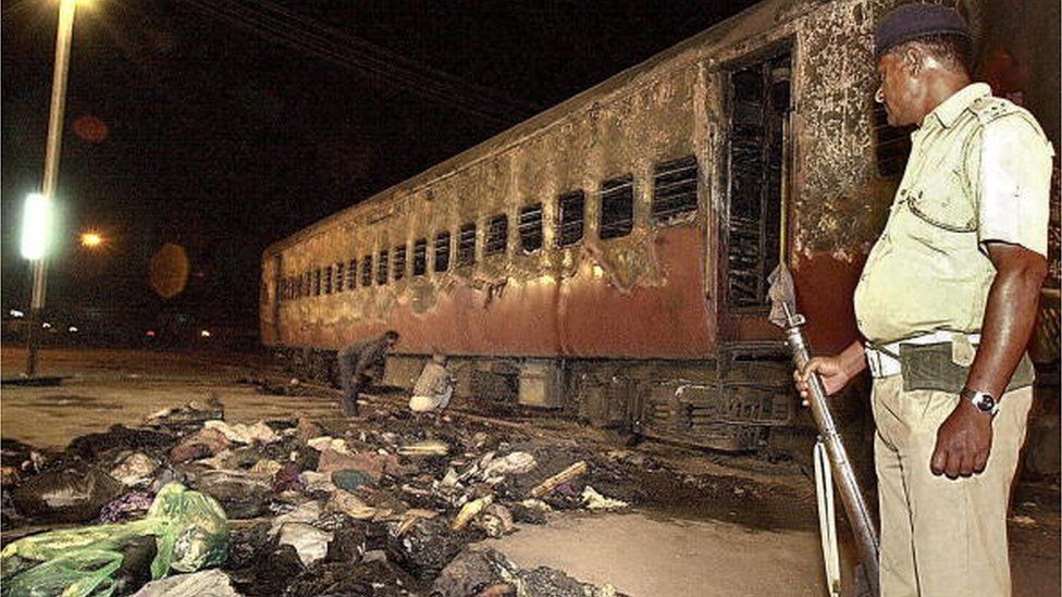 На этом снимке, сделанном 28 февраля 2002 г., индийский полицейский смотрит на сгоревший вагон поезда и вещи индуистских активистов на железнодорожной станции Годхра, примерно в 200 км от Ахмадабада