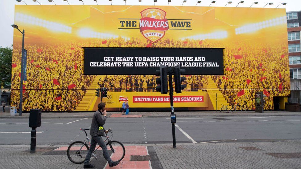 A cyclist walking his bike past a massive billboard in Cardiff