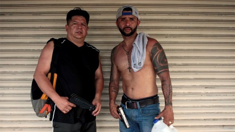 Merchants pose for a photo in front of the entrance of their business as they hold weapons to prevent looting by protesters in Managua, Nicaragua, April 22, 2018