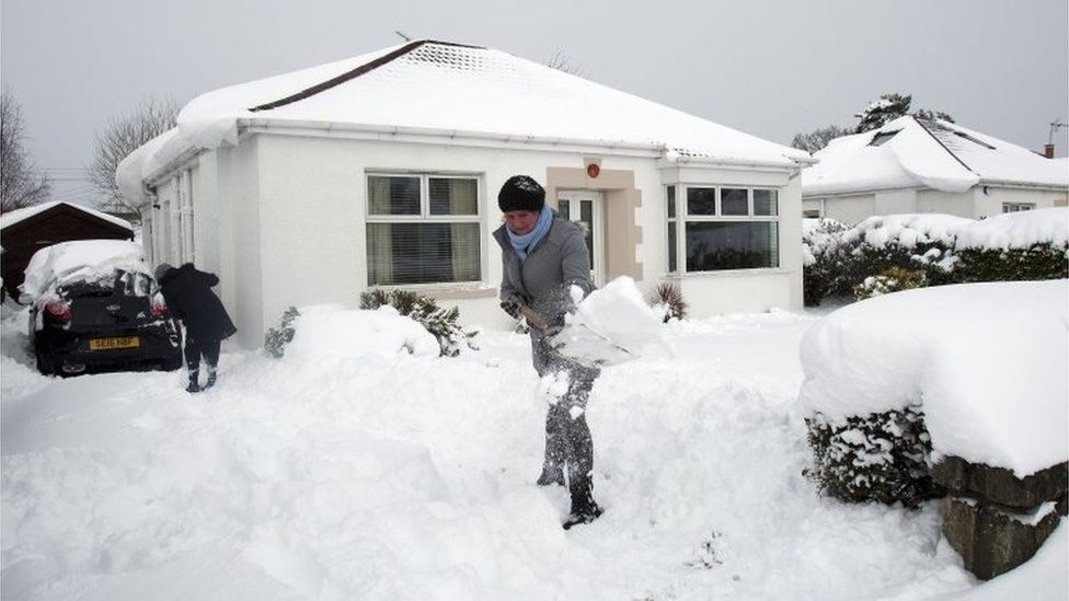 A woman clears her driveway of snow in Old Drumchapel, Glasgow