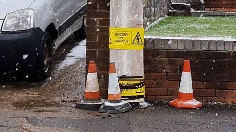 The pole with three cones around it and electric warning signs