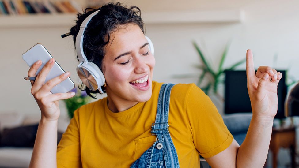 Stock image of a dancing woman wearing headphones and holding a smartphone