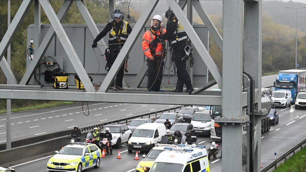 Police officers remove a protester from a motorway gantry