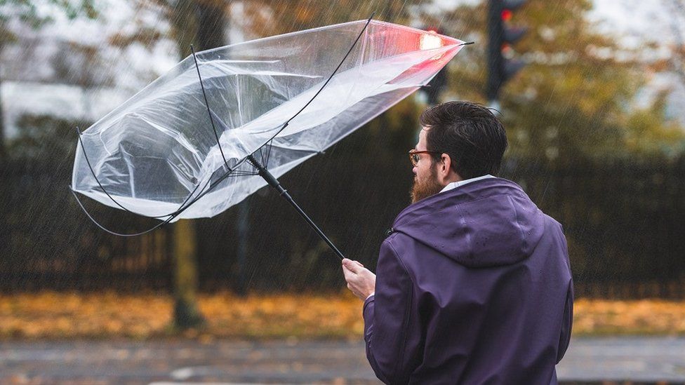 A man holds an umbrella that has blown inside out