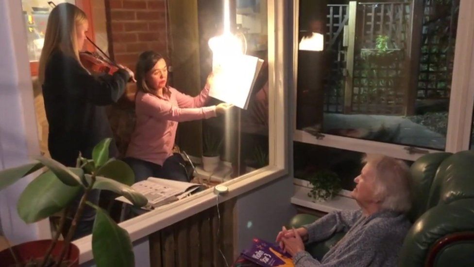 Janet Dunham, 96, teaches her great grand-daughter the violin through a screen