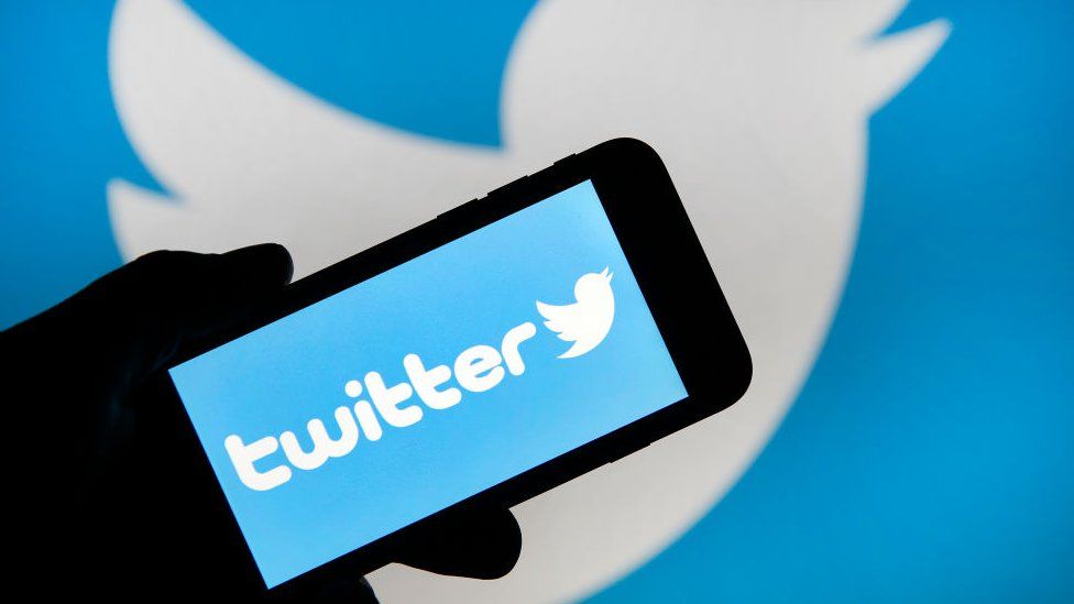 In this photo illustration the Twitter logo is displayed on the screen of an iPhone in front of a computer screen displaying a Twitter logo