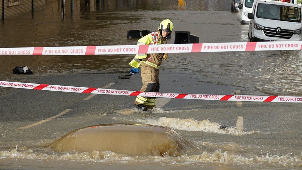 A firefighter stares at water flooding into the road