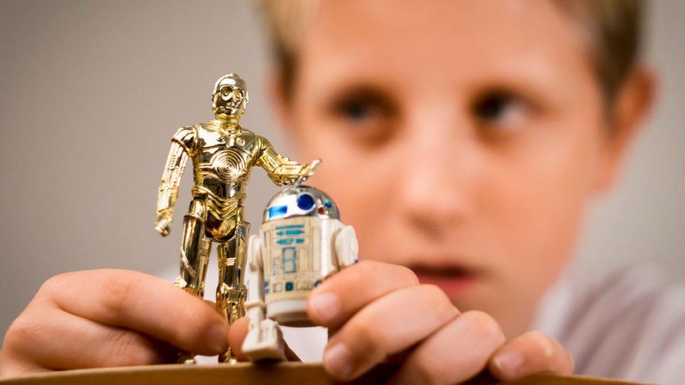 A boy playing with two Star Wars figures