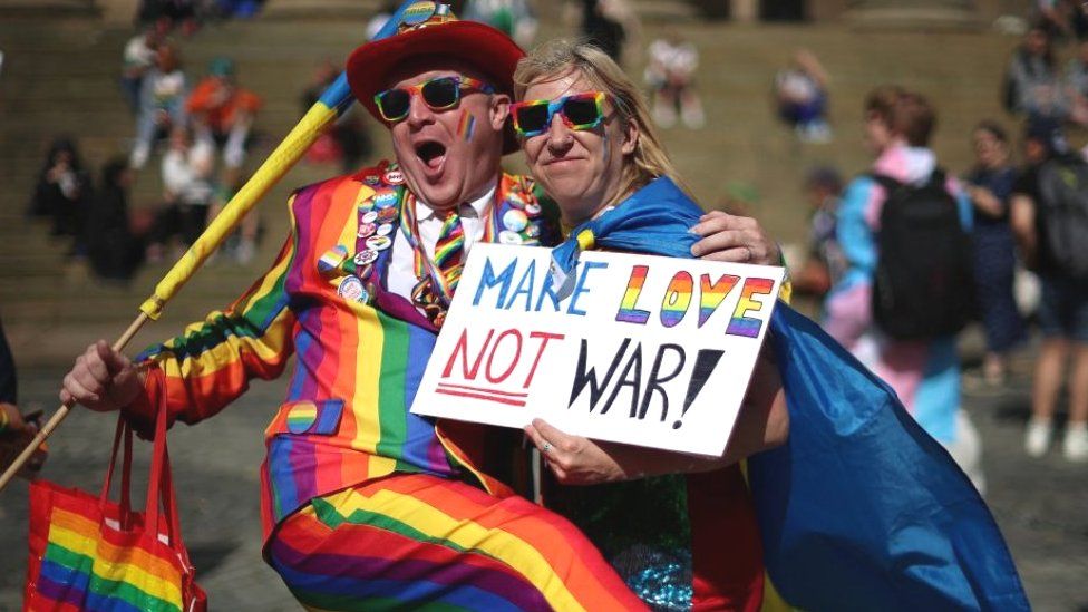 People ahead of the Pride in Liverpool parade, one holding make love, not war sign
