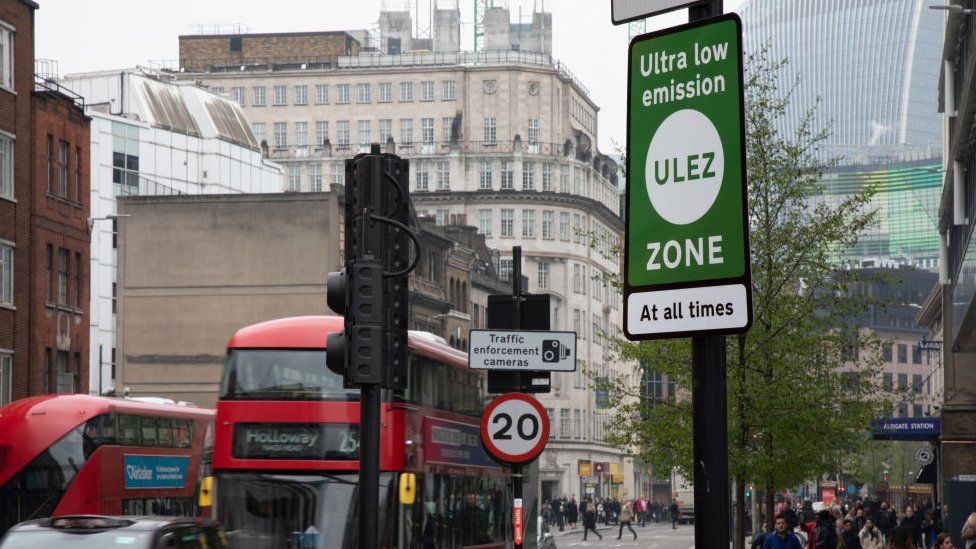 Buses and cars pass a ULEZ sign on a road in Aldgate