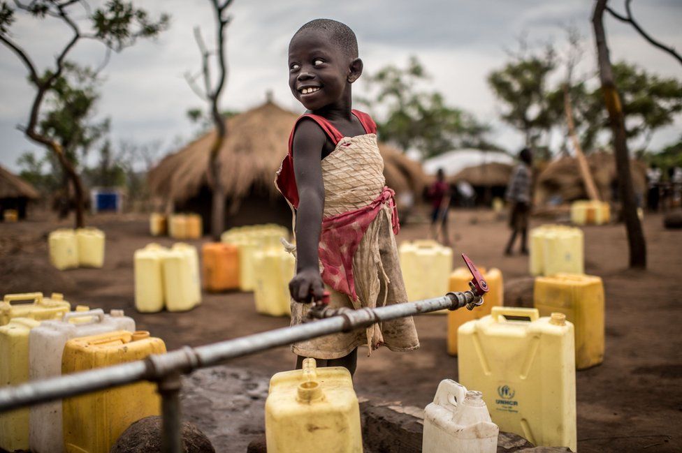 A girl smiles as she fills up her jerrycans with water