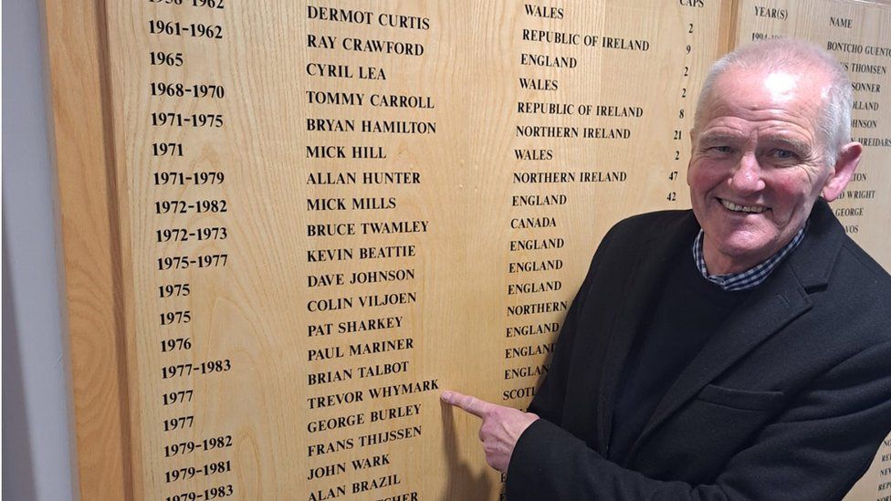 Trevor Whymark pointing at his name on the list of players to get an England cap at Portman Road