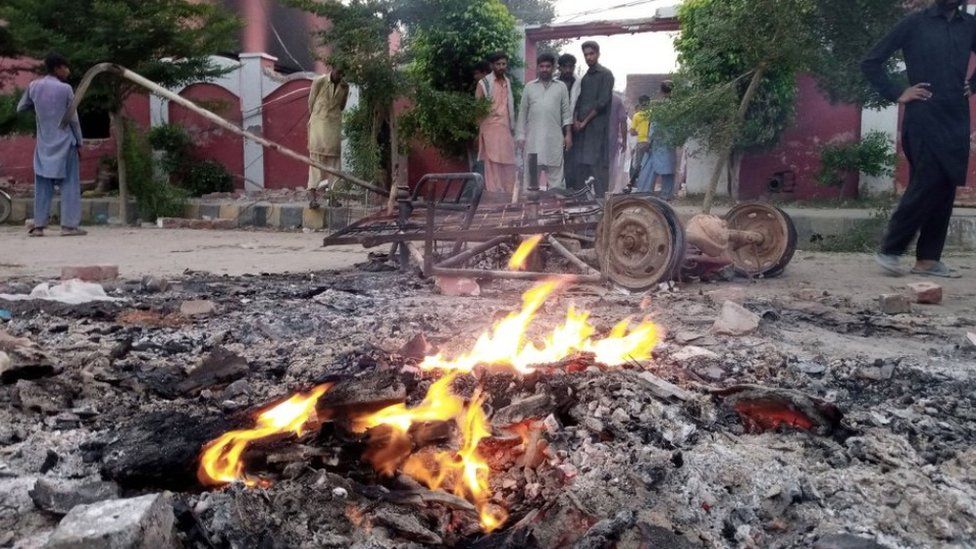 Flames rise from debris outside a Christian church after mobs burn Christian churches and homes after blasphemy allegations in Jaranwala
